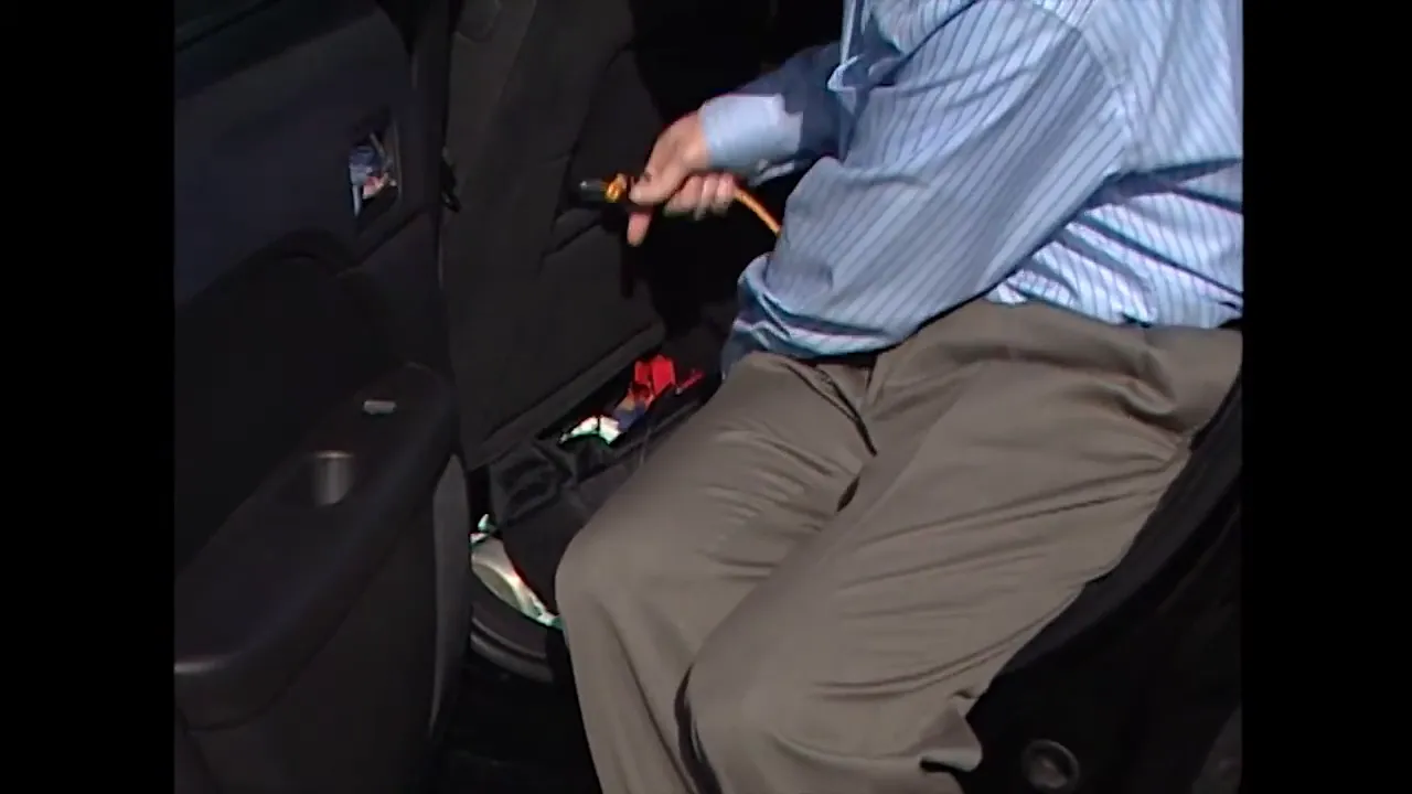person securing an oxygen tank with a seat belt in the back passenger area of a car
