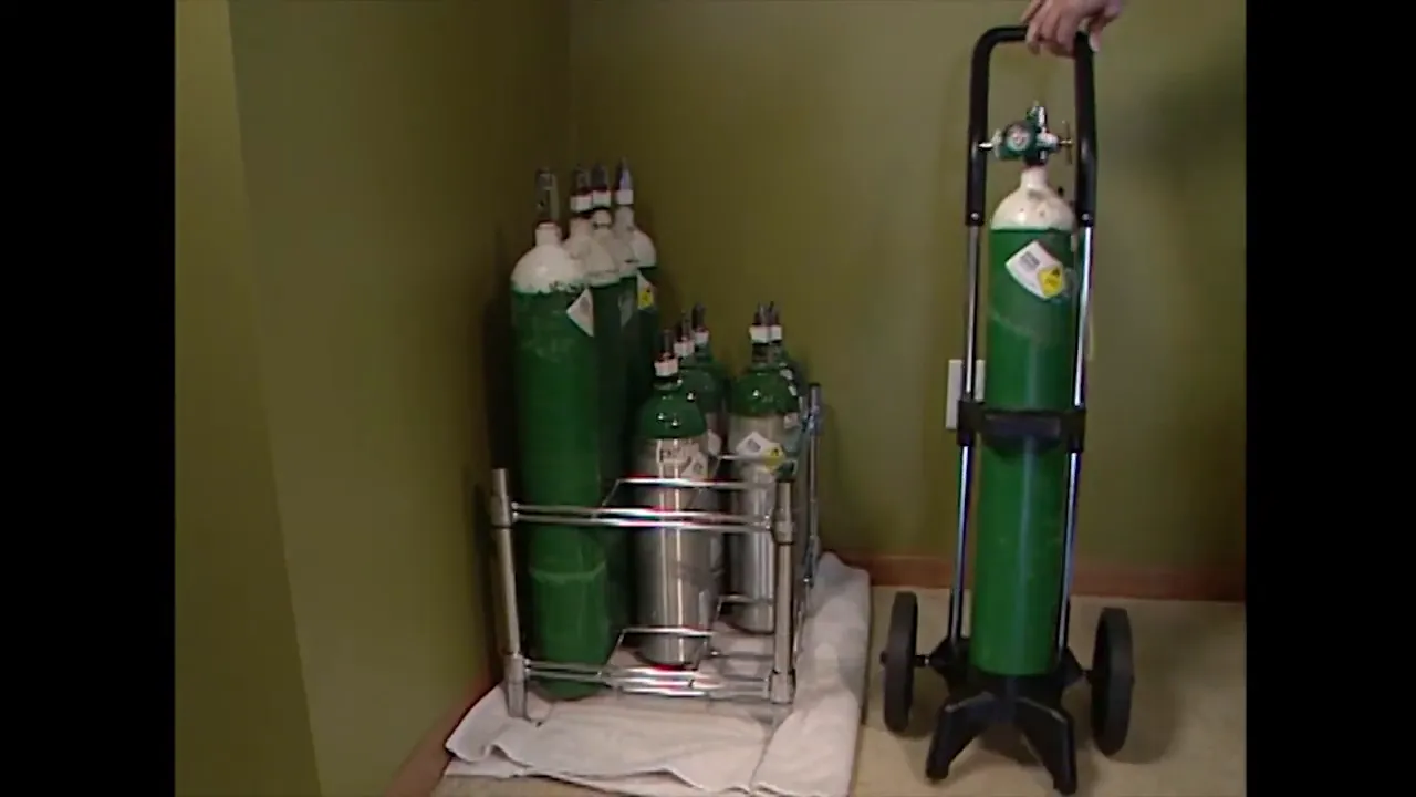 multiple oxygen tanks secured upright in a metal rack with a wheeled oxygen cart beside them