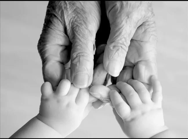 black and white photo of elderly hands touching two babies hands