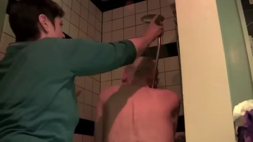 Caregiver assisting an older adult in a tiled shower using a handheld showerhead