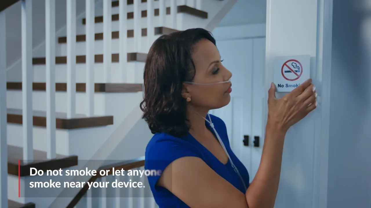 Person placing a no smoking sign on a wall with on-screen text warning not to smoke near oxygen devices