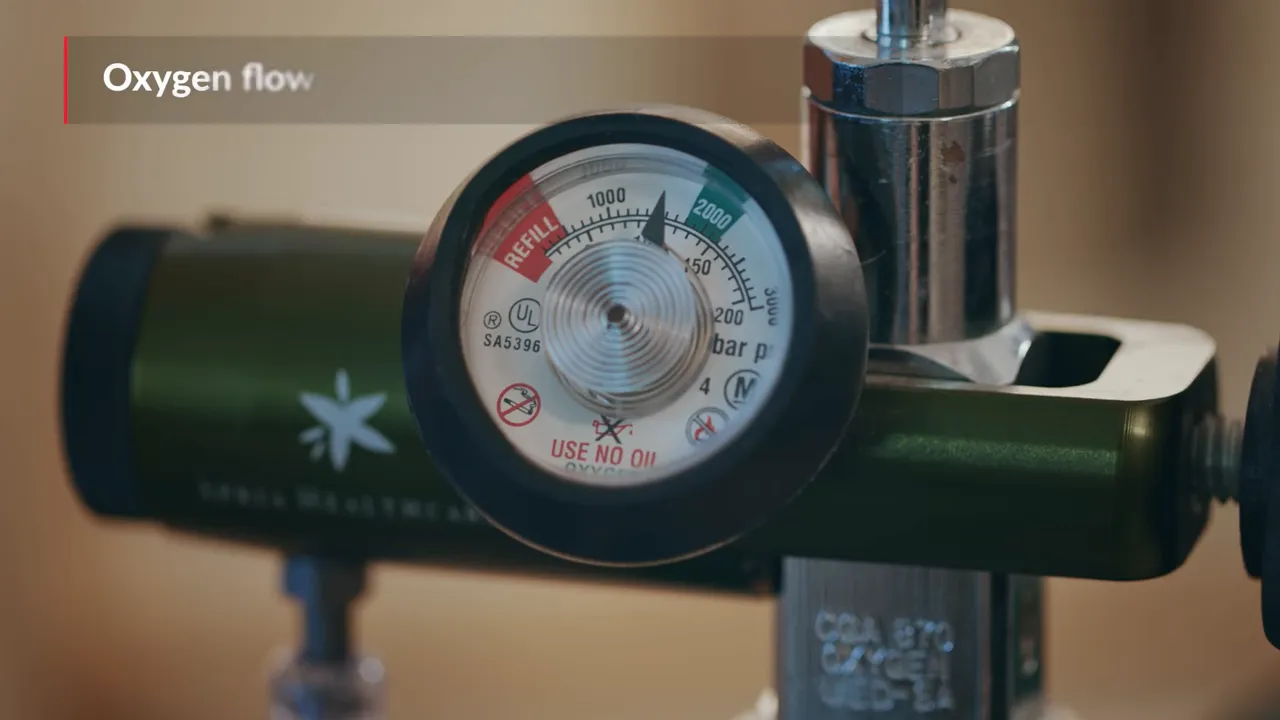 Close-up of oxygen regulator dial with on-screen text about oxygen flow rate in liters per minute