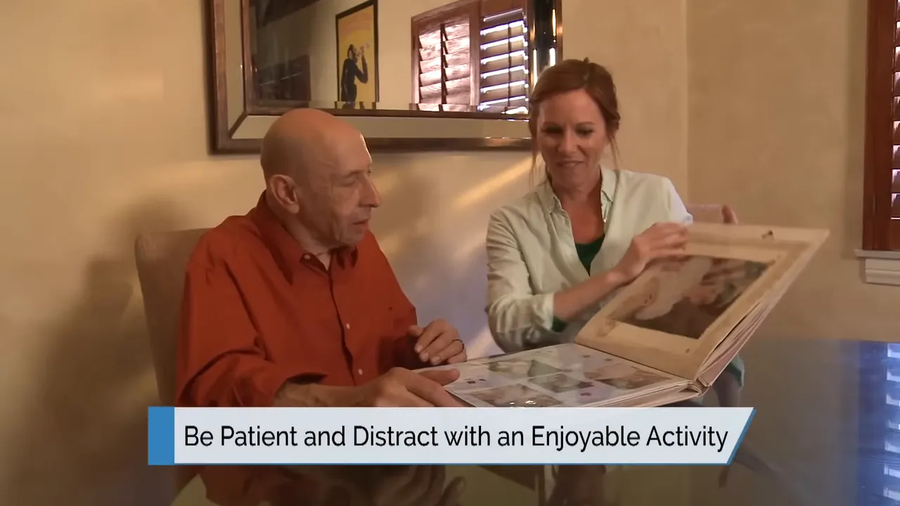 older man and caregiver looking at a photo album at a table with on-screen text be patient and distract with an enjoyable activity