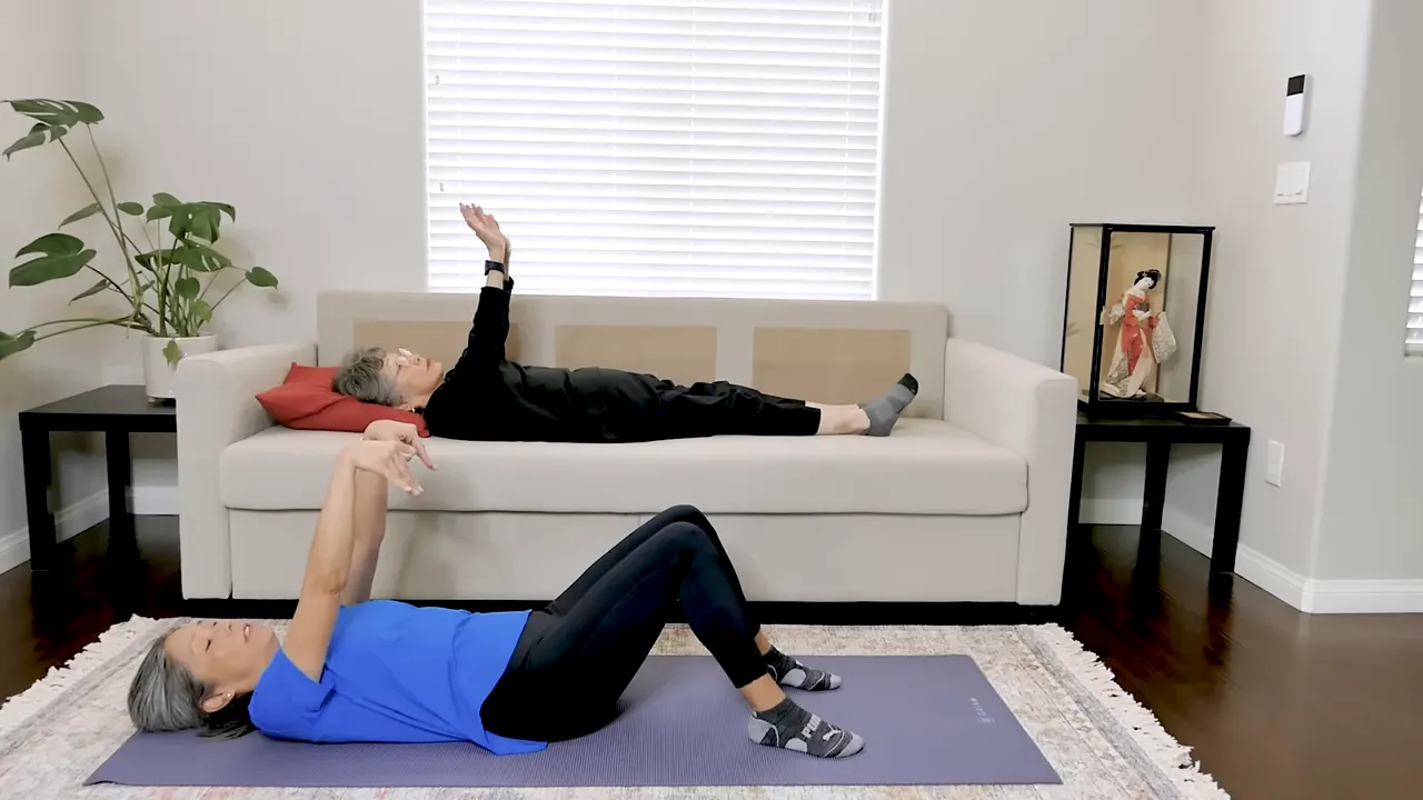 Two exercisers lying down with arms raised performing wrist and hand mobility movements