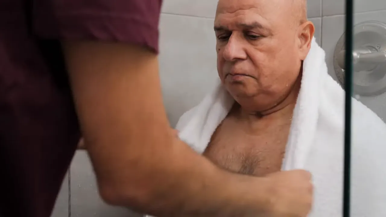 caregiver wrapping a large white towel around a seated man in the shower