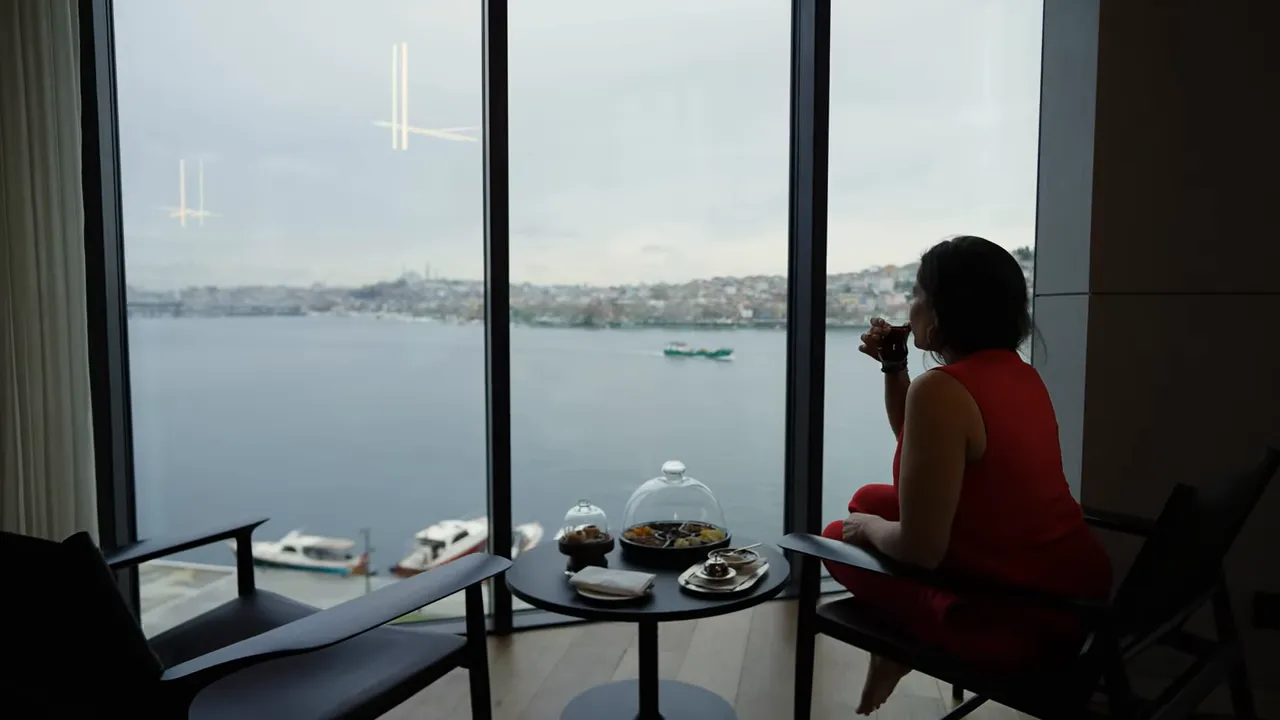 Guest enjoying in-room Turkish tea at a small table with food while looking out over the Bosphorus