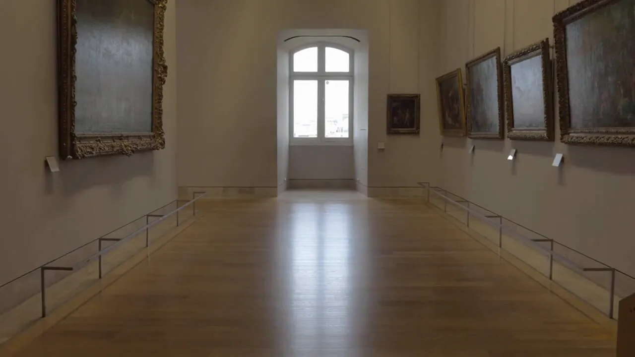 Empty gallery corridor with framed paintings on the walls and a central window, showing a calm museum interior.