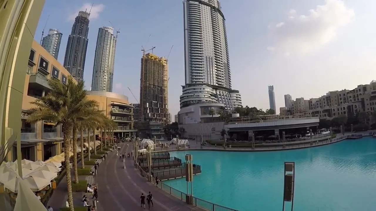 Downtown Dubai promenade with turquoise water, palm trees and tall buildings, showing a pedestrian route for gallery visits
