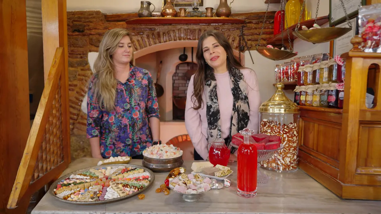 Wide view of a traditional Turkish confectionery counter with trays of lokum, jars and two people behind the counter