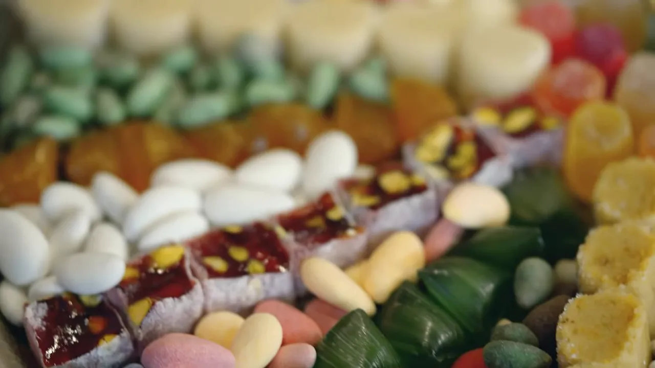Close-up of white sugar-coated almonds next to cubed lokum and assorted colorful candies on a tray.