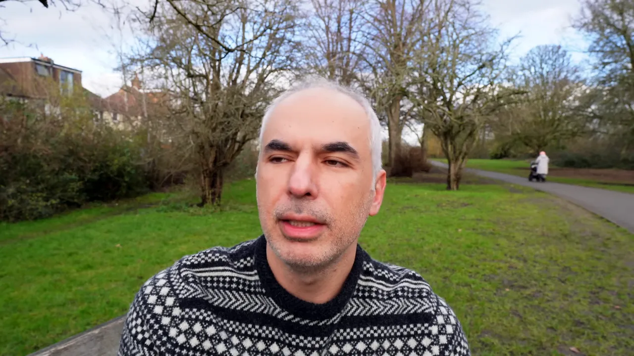 Parkta konuşan sunucu, arka planda bebek arabasıyla y&uuml;r&uuml;yen kişi