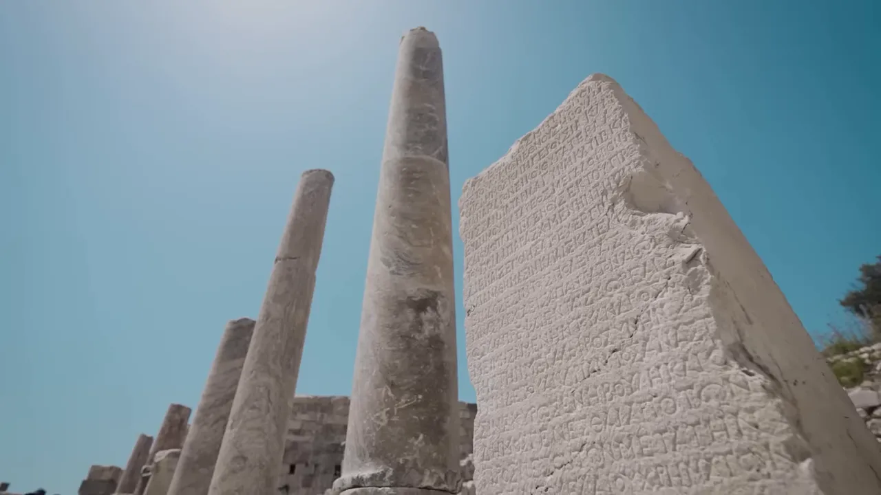 Wide shot of tall marble columns and an inscribed stone stele at Patara against a clear blue sky.