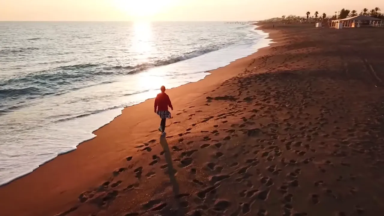 Lara Plajı kıyısı, bir kişinin yürüdüğü altın rengi kumlar ve deniz dalgaları