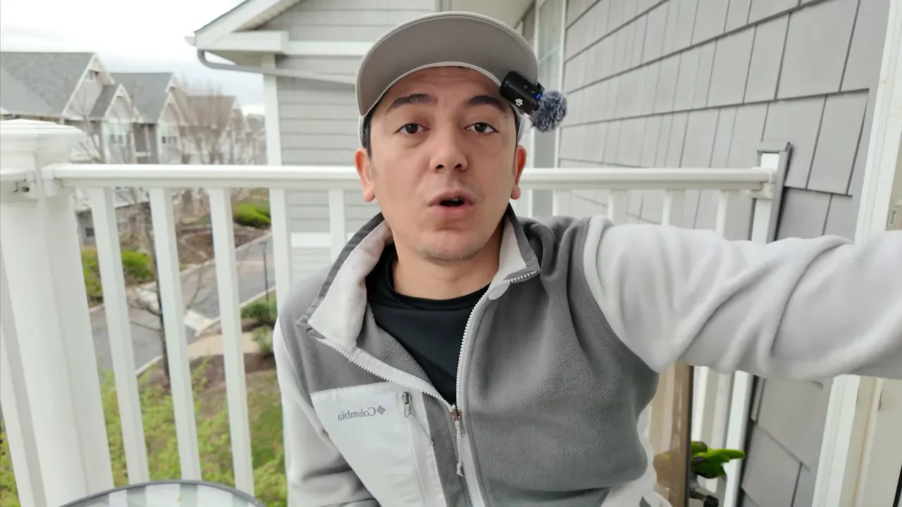 Balkonda oturan konuşmacı şapka ve mikrofonla konuşuyor, elini uzatıyor