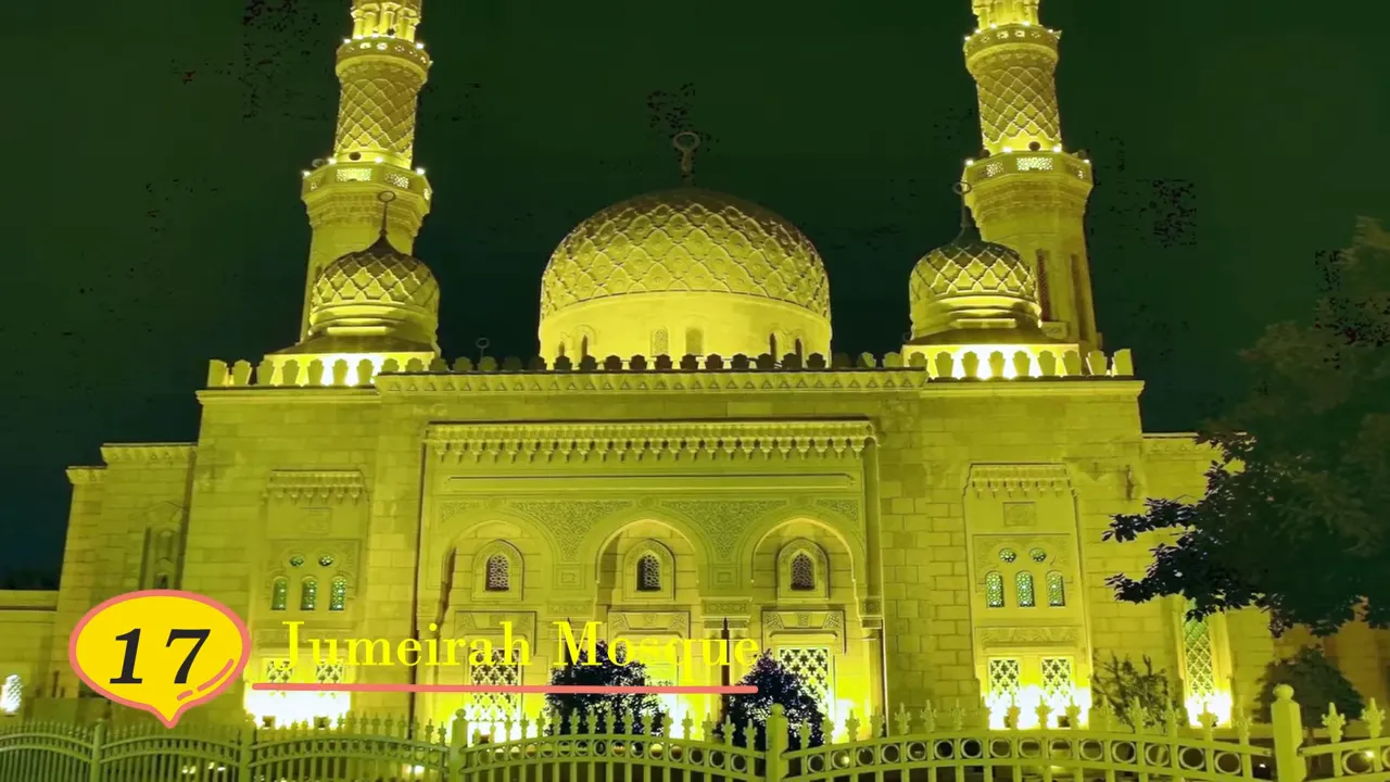 Jumeirah Mosque fa&ccedil;ade and domes lit up at night with fence and trees in the foreground