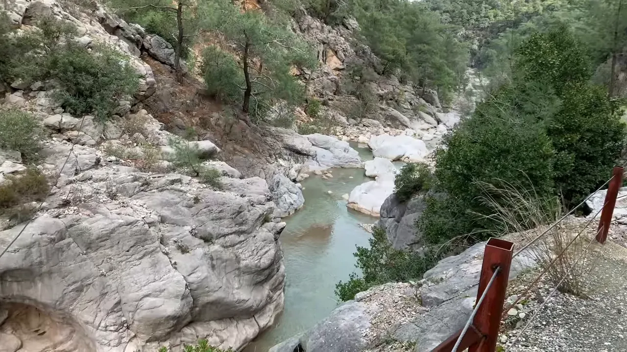 Turquoise canyon river with smooth white rocks and a safety railing along the path