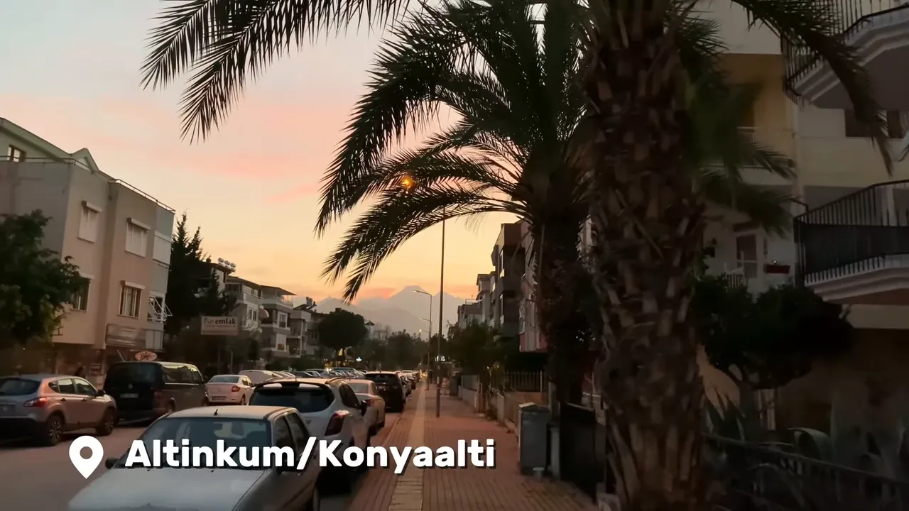 Palm-lined street at sunset in Konyaaltı with parked cars and distant mountains