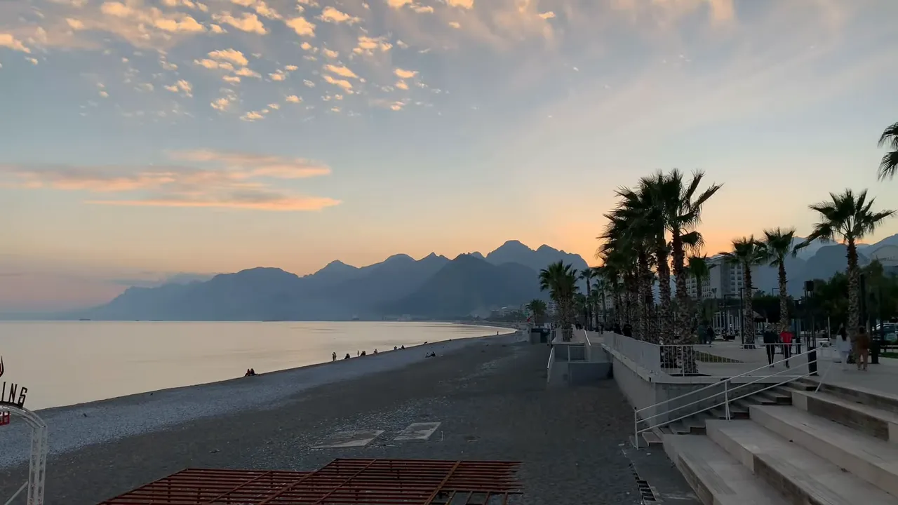 Lara Beach shoreline with palm trees, beachfront hotels and mountains at sunset