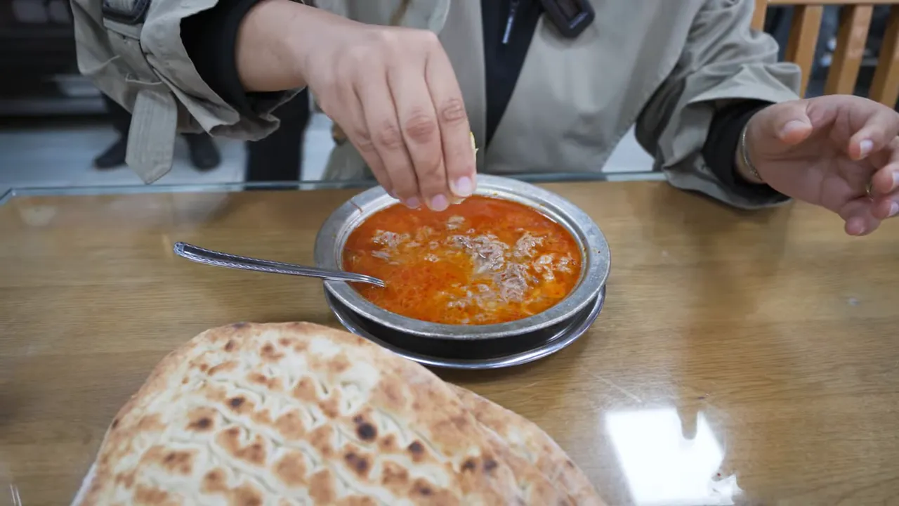 lemon being squeezed over a bowl of biran lamb-and-rice soup with flatbread