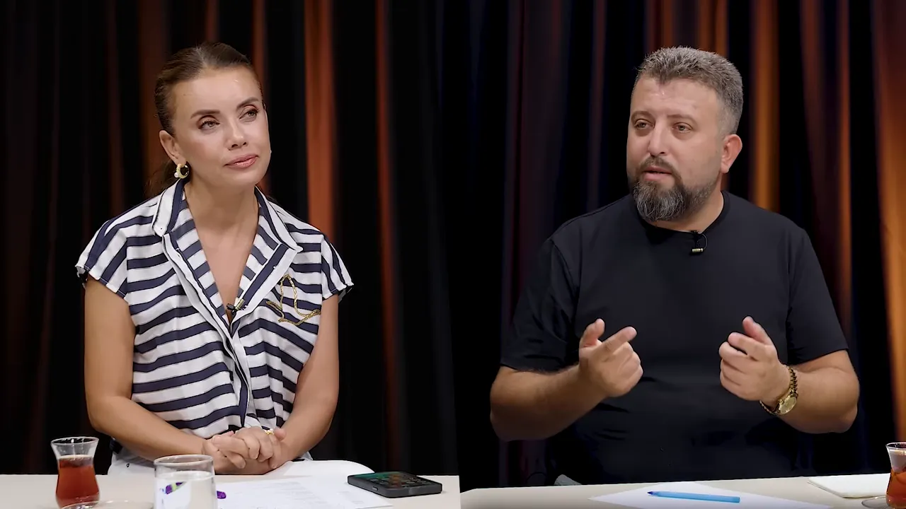 Stüdyo masasında evraklar, kalem ve telefon önünde konuşan iki kişi; elleriyle açıklama yapıyorlar.