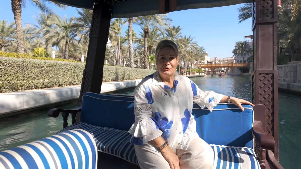 Souq Medinat abra teknesinde oturan yolcu, arkada kanal, k&ouml;pr&uuml; ve palmiye ağa&ccedil;ları