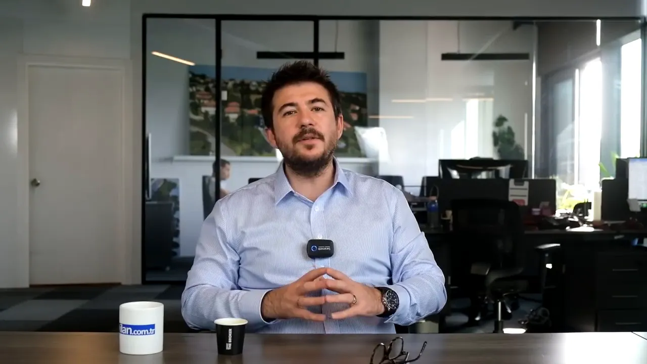 Presenter in an office environment speaking to camera, clear mid-shot with hands visible.