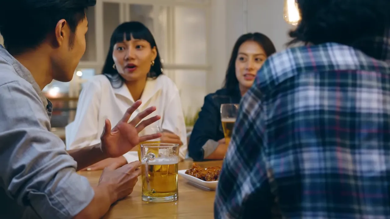 Small group of people conversing at a table with beer mugs and shared dishes