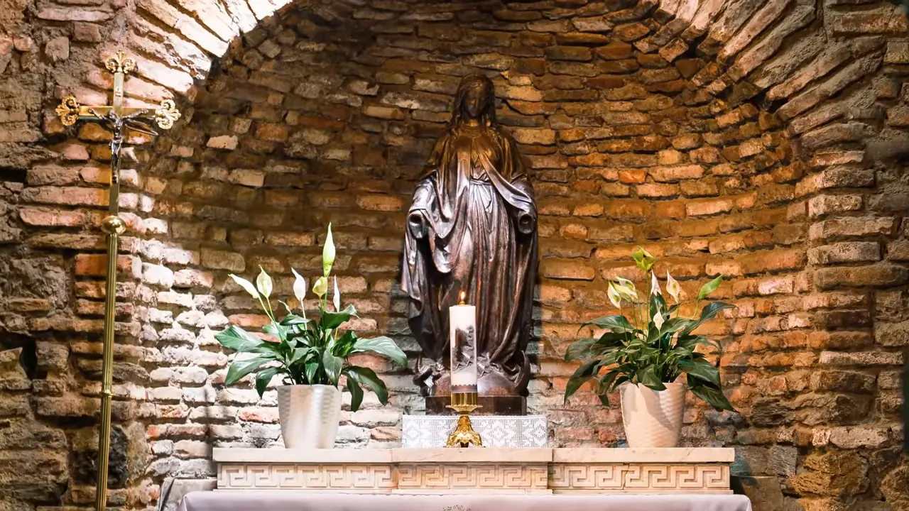 statue of the Virgin Mary on an altar inside a brick chapel alcove with plants and candle
