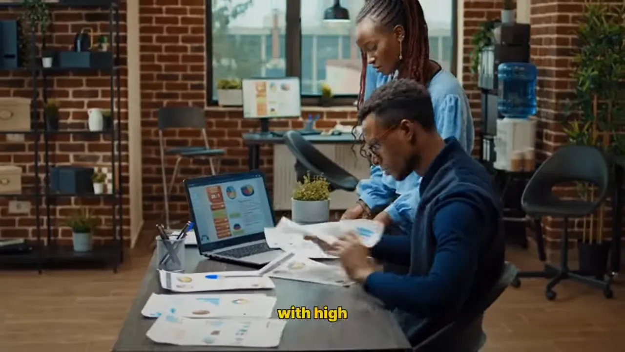 two coworkers reviewing printed budget papers and a laptop at a desk