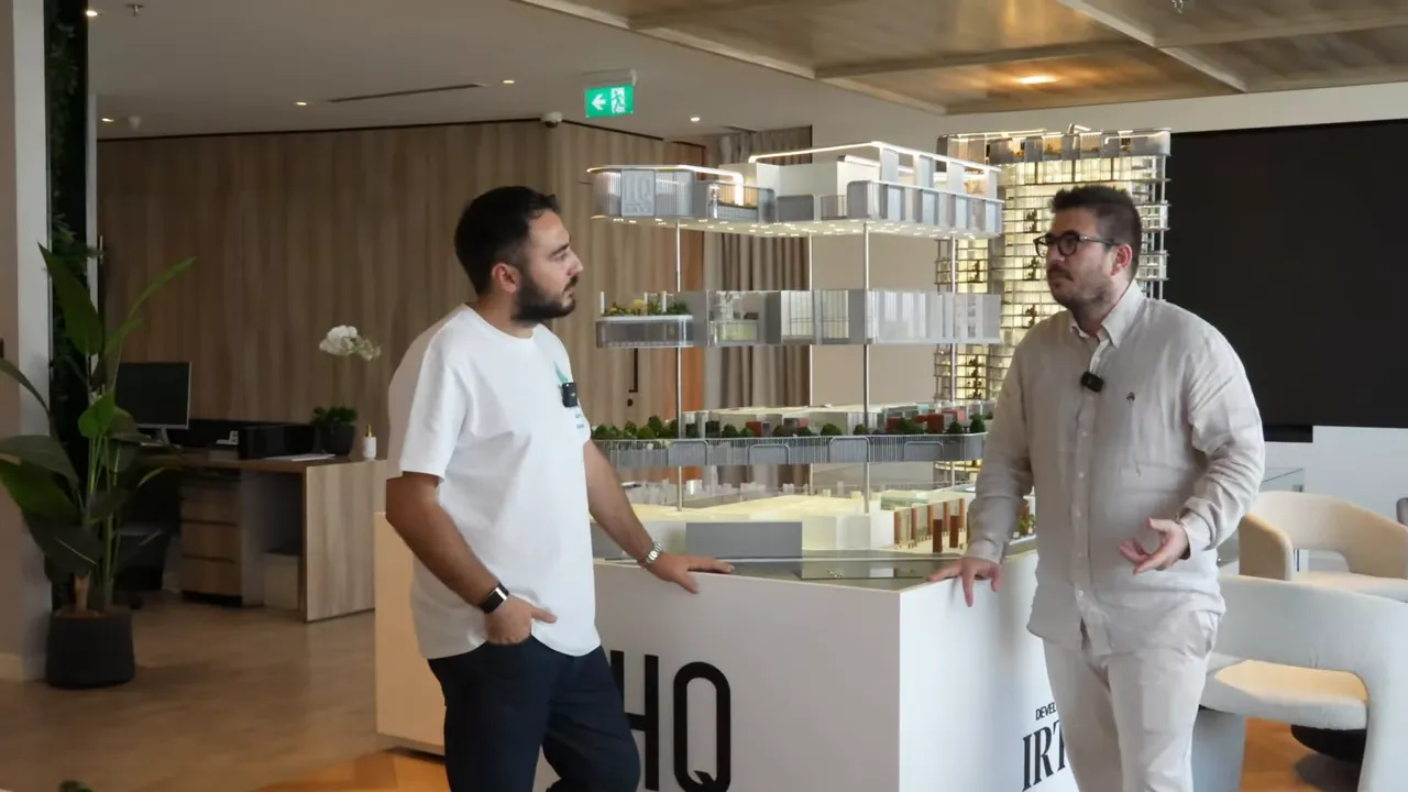 Ofis projesi maketi merkezde; iki konuşmacı maket &ouml;n&uuml;nde, arka planda lounge ve oturma alanları a&ccedil;ık&ccedil;a g&ouml;r&uuml;l&uuml;yor.