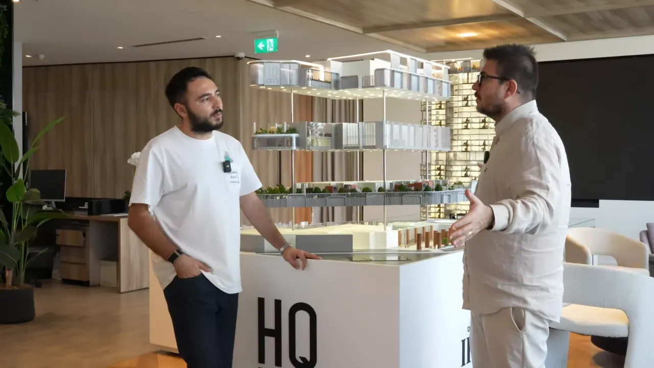 Ofis proje maketi merkezde; iki konuşmacı maket etrafında duruyor, maket detayları ve ortak alanlar net g&ouml;r&uuml;n&uuml;yor.