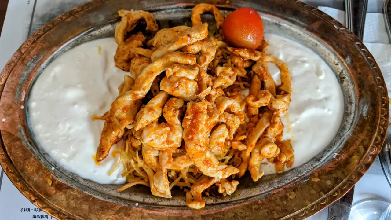 Top-down shot of çökertme chicken with yogurt and crispy shredded potatoes on a metal platter