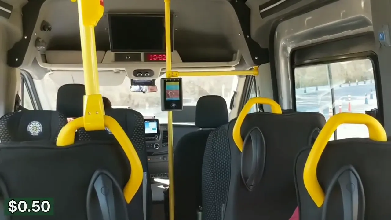 Interior of a Bodrum shared minivan (dolmuş) showing black seats with yellow handrails and a $0.50 fare graphic in the corner
