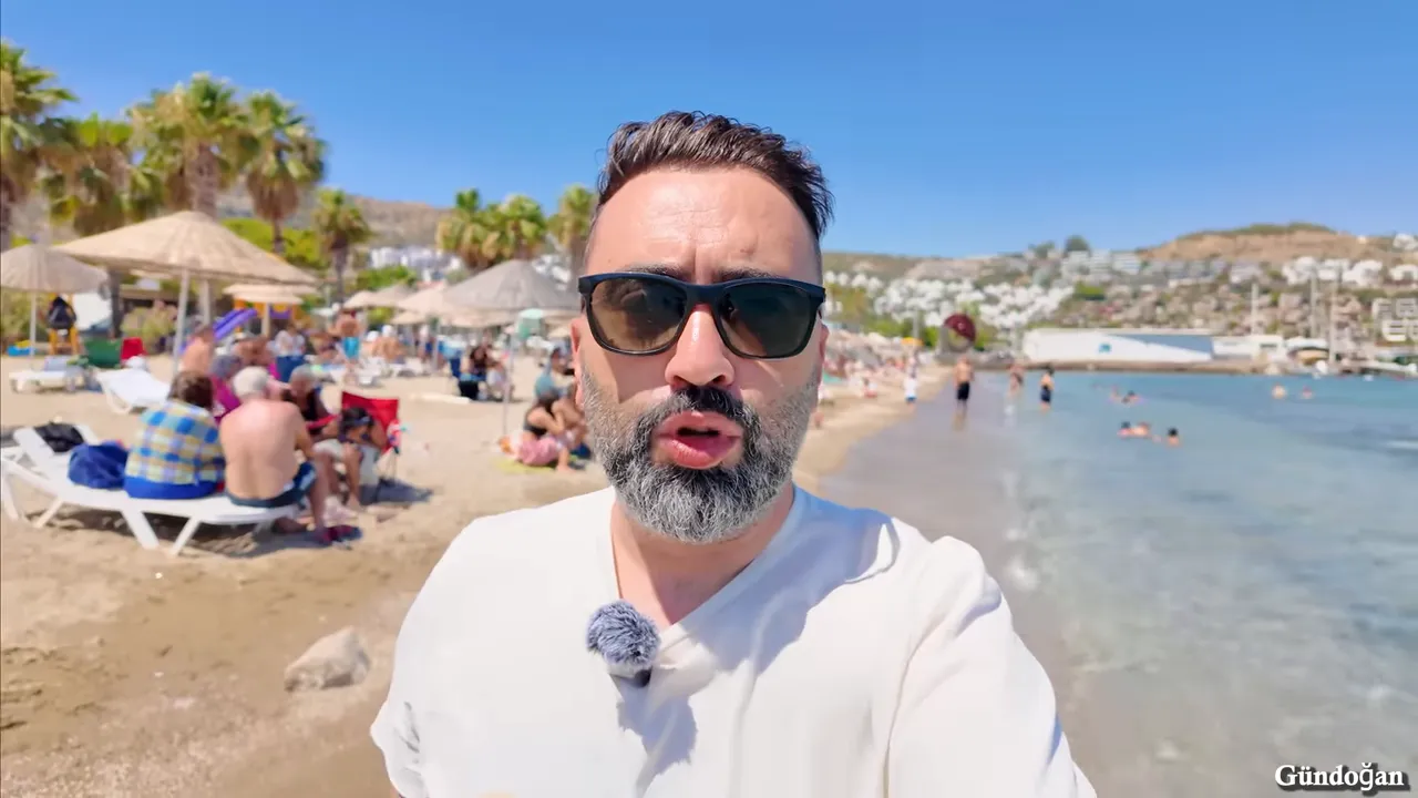 Palmiyeler, plaj şemsiyeleri ve sahilde güneşlenenlerle birlikte kıyı hattını gösteren geniş açı sunucu görüntüsü