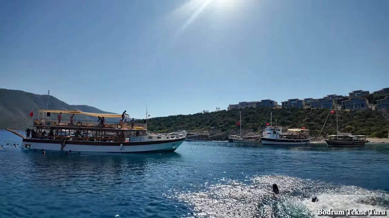 Tekne turu sırasında görülen guletler, yüzücüler ve güneşte parlayan turkuaz deniz