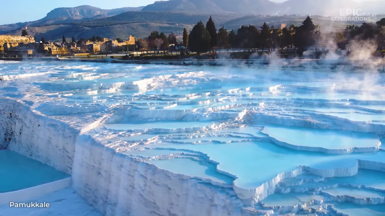 Pamukkale travertine terraces with steaming thermal pools and ancient Hierapolis ruins in the background