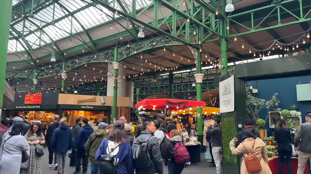interior of Borough Market under a glass roof with decorative ironwork, stalls and shoppers