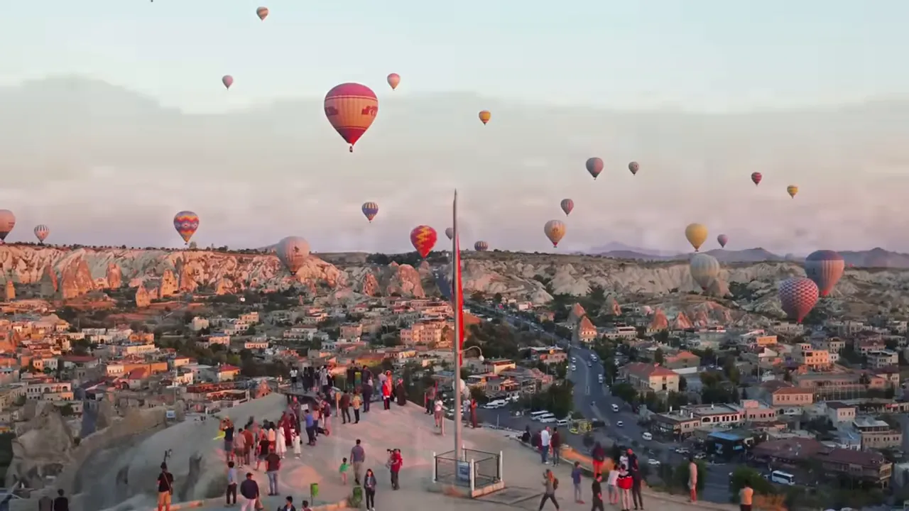 Hot air balloons over Cappadocia rock formations with tourists watching from a viewpoint at sunrise