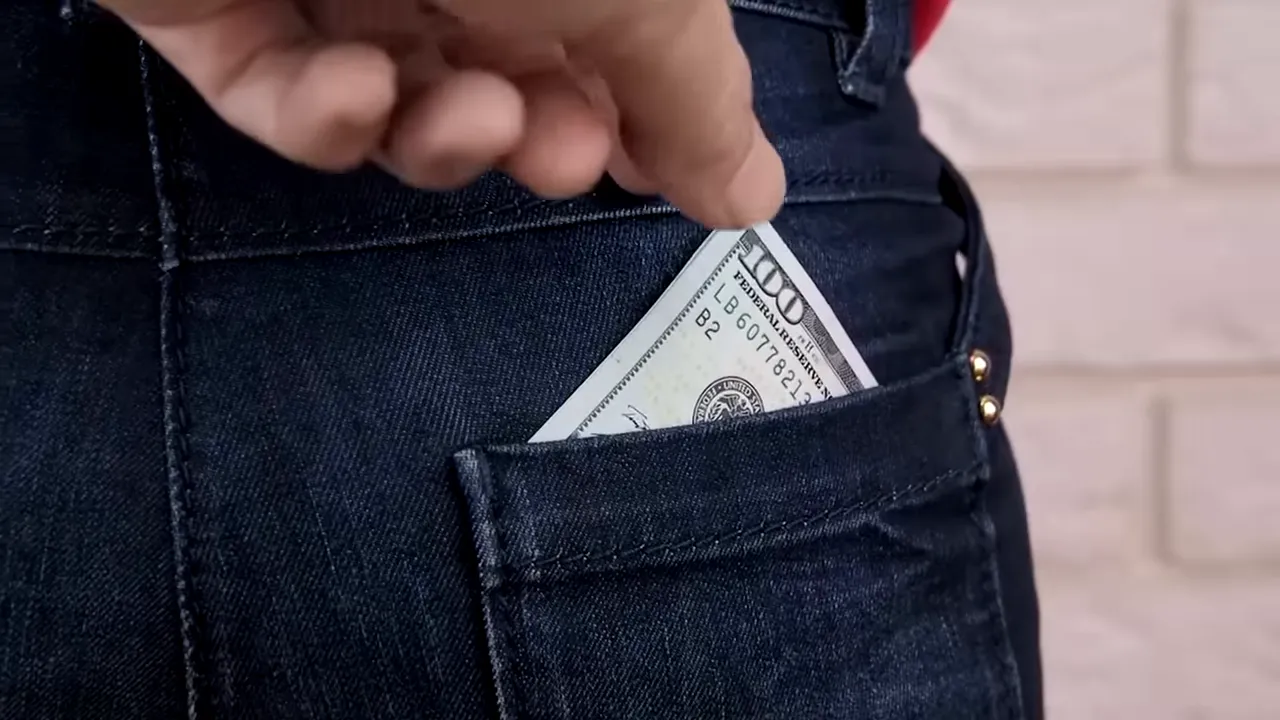 Hand placing a US dollar bill into a back pocket of dark jeans illustrating pickpocket risk