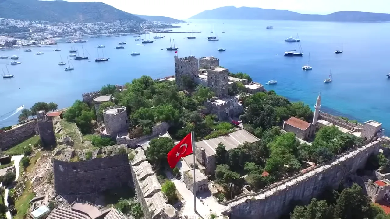 Aerial view of a seaside castle with a Turkish flag and boats in the bay