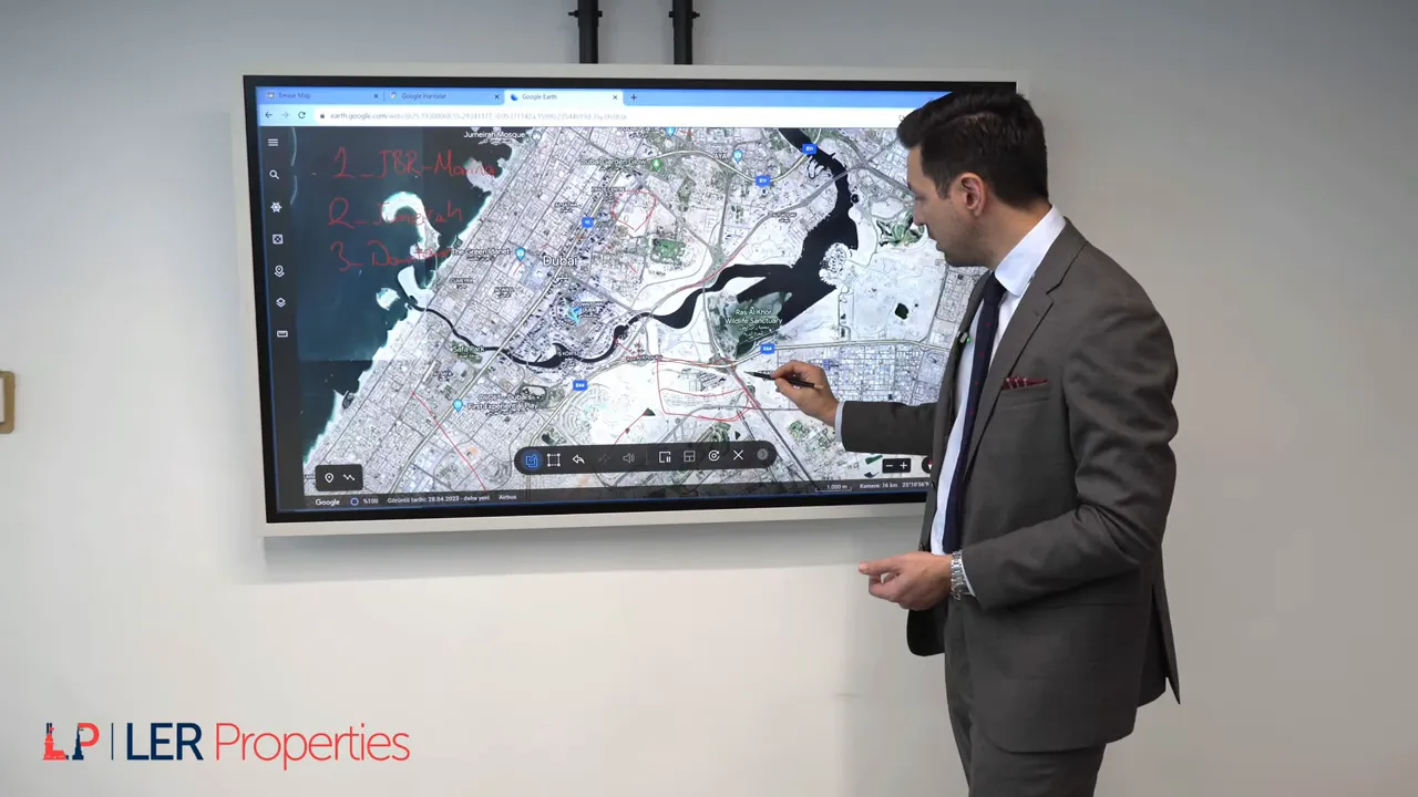 Sunum yapan kişi ekranda Dubai uydu haritasını kalemle işaret ediyor; Ras Al Khor Wildlife Sanctuary g&ouml;r&uuml;n&uuml;r