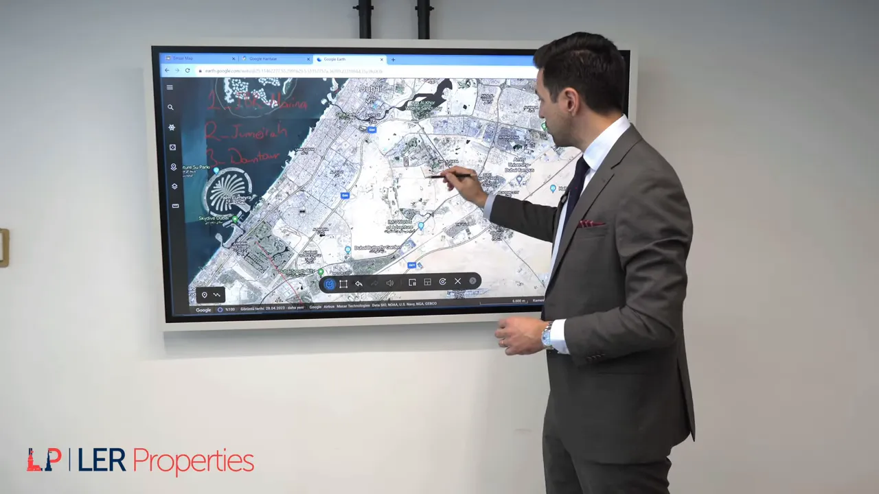 Sunum yapan kişi kalemle Dubai uydu haritasında District One b&ouml;lgesine işaret ediyor; harita net ve okunaklı.