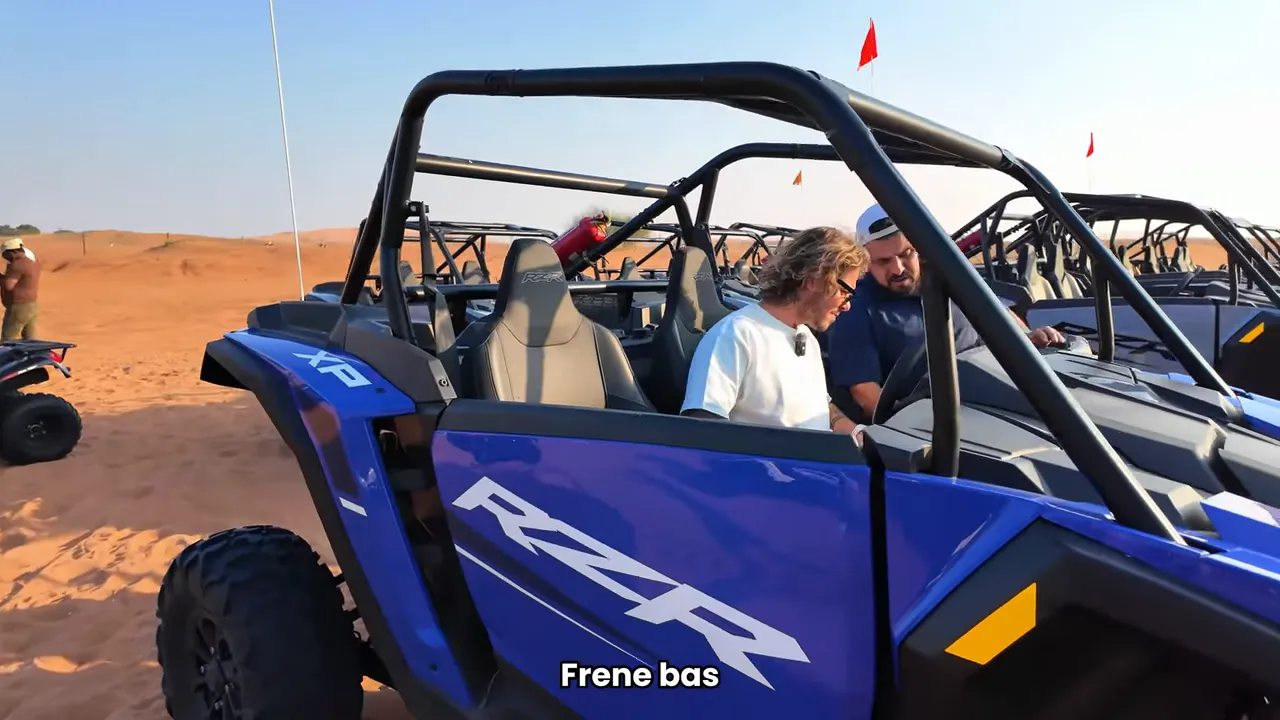 Mavi RZR marka buggy yan profilden, &ccedil;&ouml;l&uuml;n ortasında park halinde; s&uuml;r&uuml;c&uuml; brifingi sahnesi.