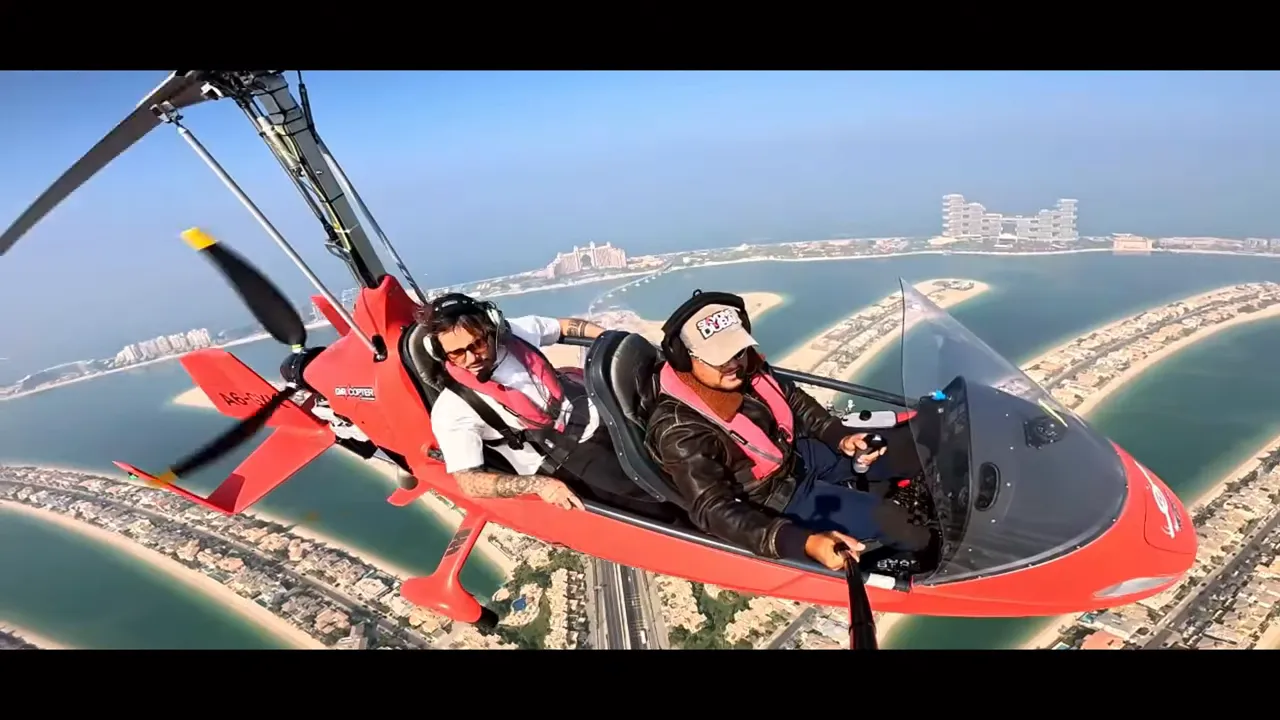 Kırmızı gyrocopter kabininde pilot ve yolcu, altında Palm Jumeirah adaları ve kanalların belirgin g&ouml;r&uuml;n&uuml;m&uuml;.