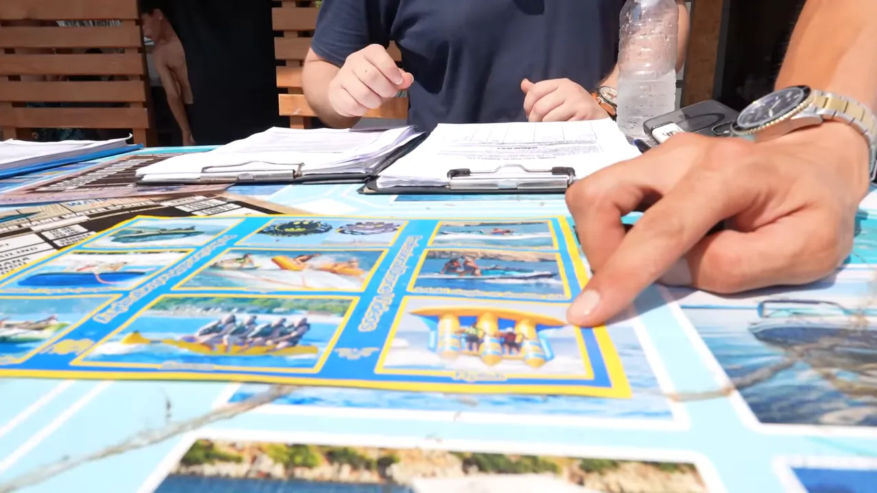 Masada yakın çekim su sporları broşürü ve bir kişinin parmağı ile gösterme hareketi.