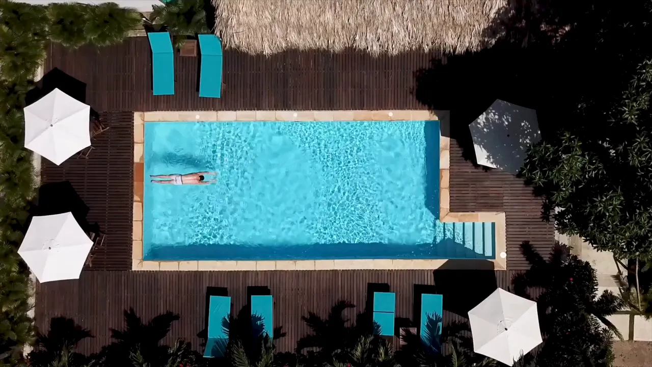 Aerial view of a clear community swimming pool with sun loungers and umbrellas.