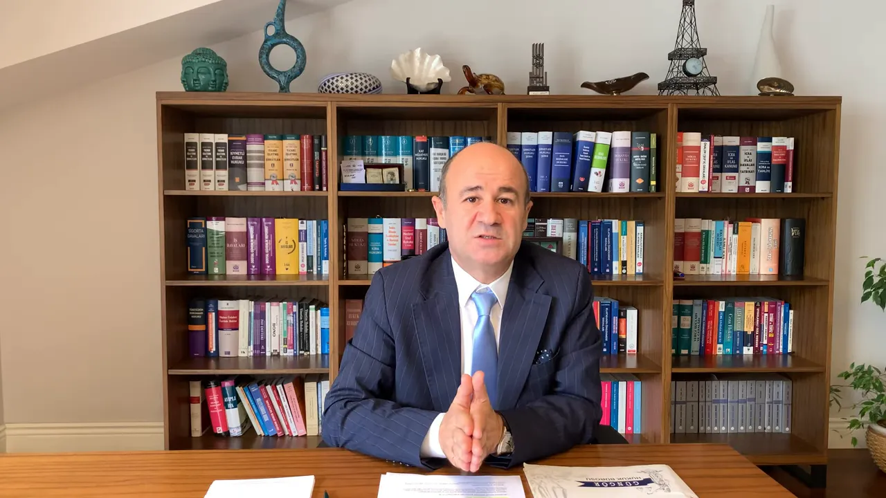 Kitaplık arkasında oturan uzman, masada evraklar ve elleri &ouml;nde a&ccedil;ıklama yapıyor