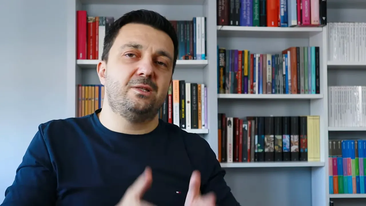 Konuşmacı kitaplık önünde satın alma kontrol listesini anlatıyor, net ve temiz kare