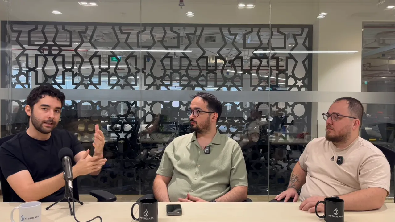 Soldaki konuşmacı el hareketleriyle maliyetleri a&ccedil;ıklıyor, diğer iki konuşmacı dinliyor