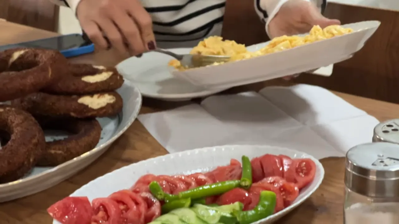 Close-up of a Turkish breakfast showing simit (sesame ring bread), scrambled eggs, sliced tomatoes and green peppers on plates.